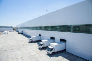 A warehouse with box trucks in the loading position at the loading dock of the warehouse.